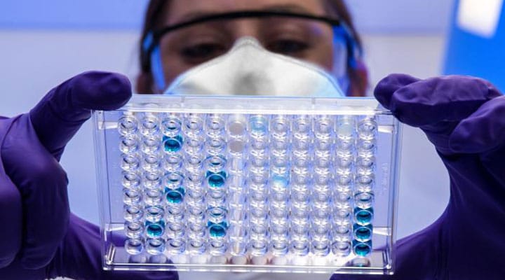 Researcher with gloves and mask looking at sample tray