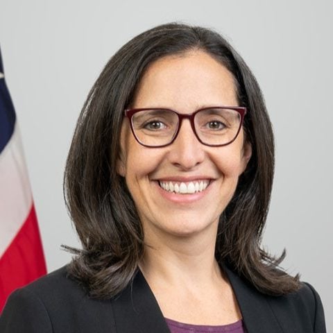 Andi Lipstein Fristedt, MPA, is the Deputy Director/Chief Strategy Officer. An American flag is behind her.