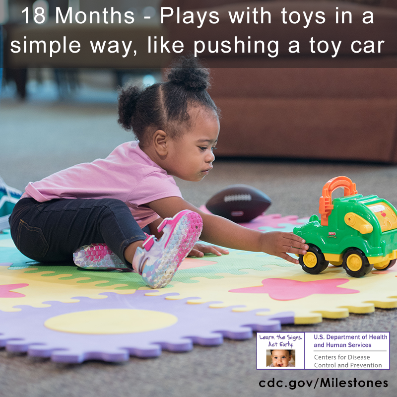 The girl in this photo is reaching out and playing with a green and yellow toy car.