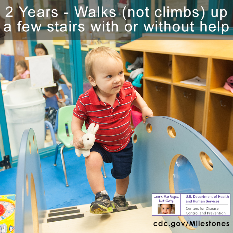 The boy in this photo is wearing a red shirt and is walking up a few steps without help, a 2 year milestone.