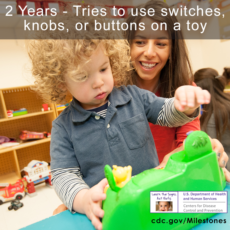 The child in this photo is trying to use a button on a green toy, a 2 year milestone.