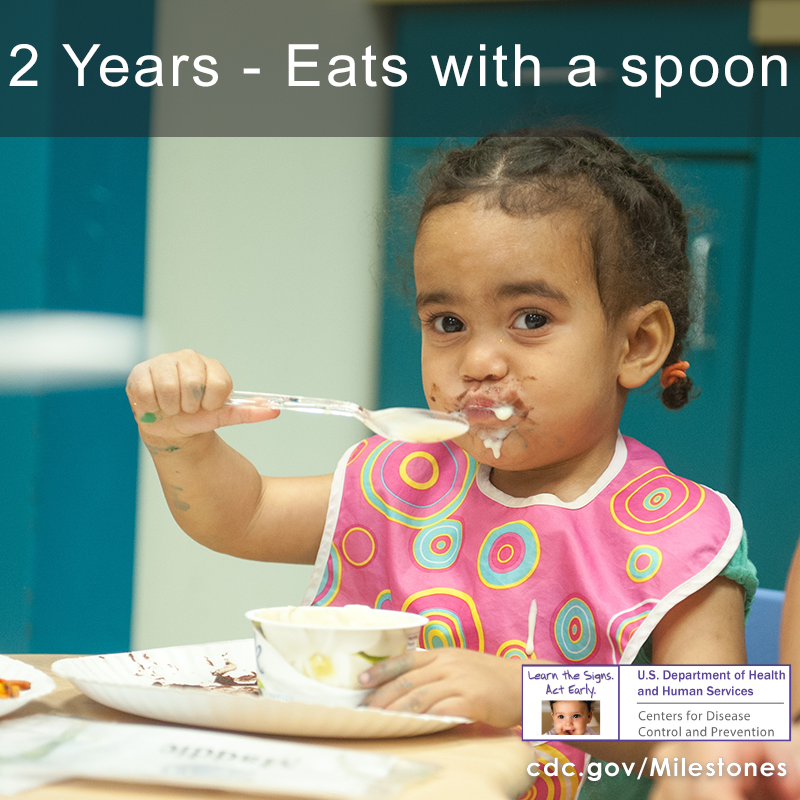 The girl in this photo is eating with a spoon, a 2 year milestone.