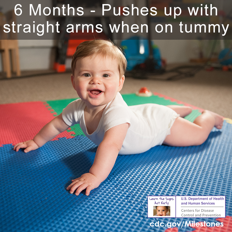 Baby is laying on belly and pushing up with arms while smiling at the camera.