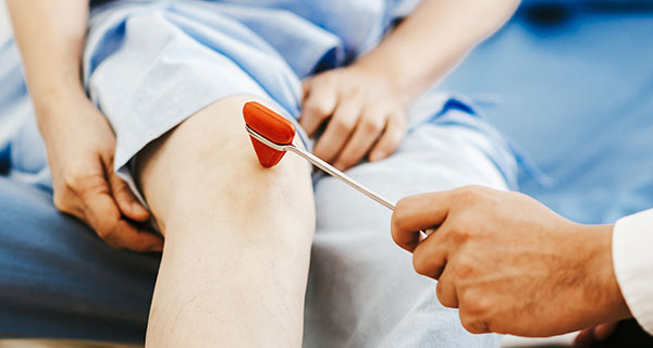 Doctor using reflex hammer on patient knee.