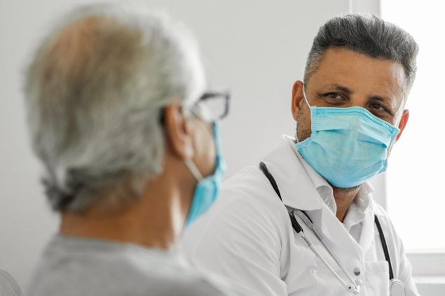 Doctor talking to a senior patient at home Masked HCP with masked patient