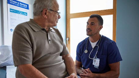 Spanish Healthy Habits Image shows Hispanic healthcare professional speaking to older Hispanic man in healthcare setting.
