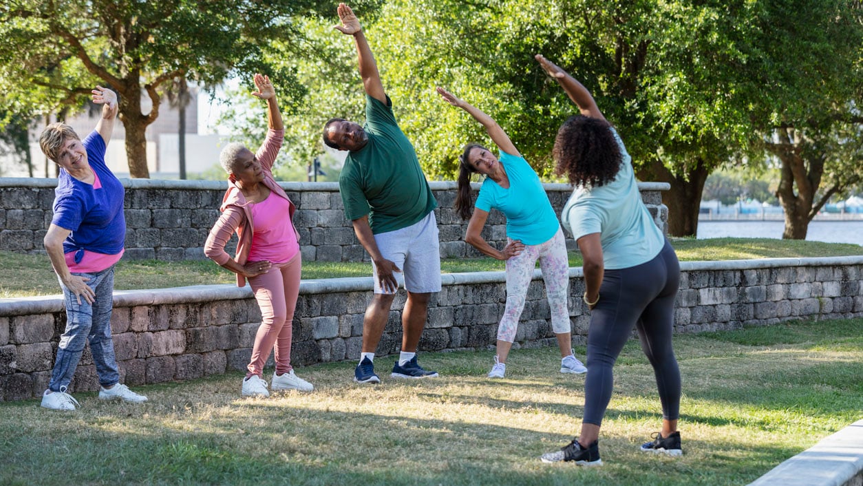 Group exercise class with instructor at park, stretching People stretching in the park as a group