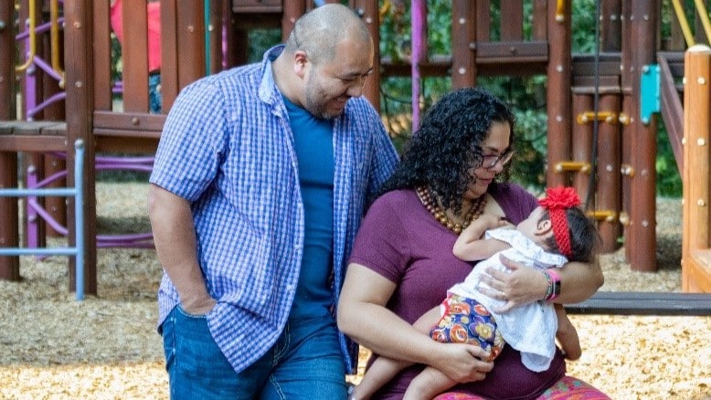 — title missing — Man and woman at a park while woman breastfeeds a baby.