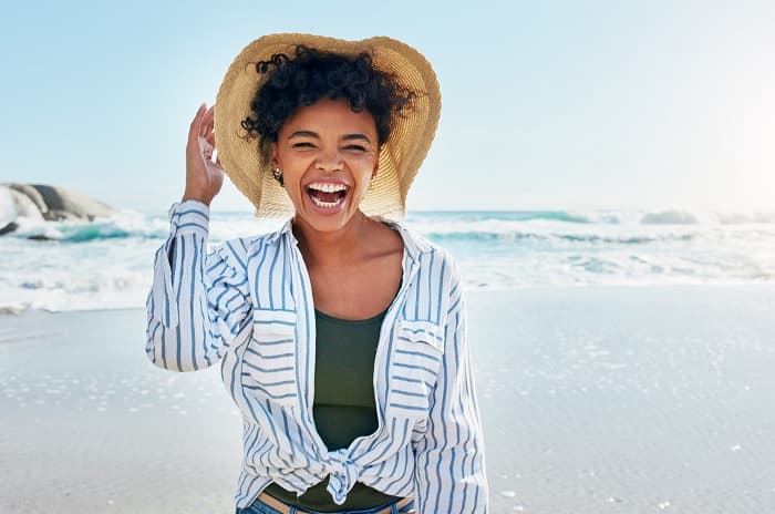 Photo of a woman at a beach. She is wearing a long-sleeved shirt and a hat with a wide brim.