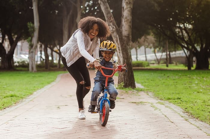 Social Determinants of Health Photo of a woman teaching son to ride a bicycle at a park