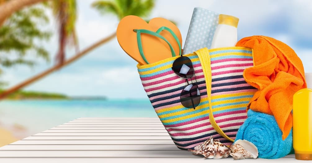 Photo of a colorful tote bag containing sunscreen, sunglasses, a hat, towels, and shoes