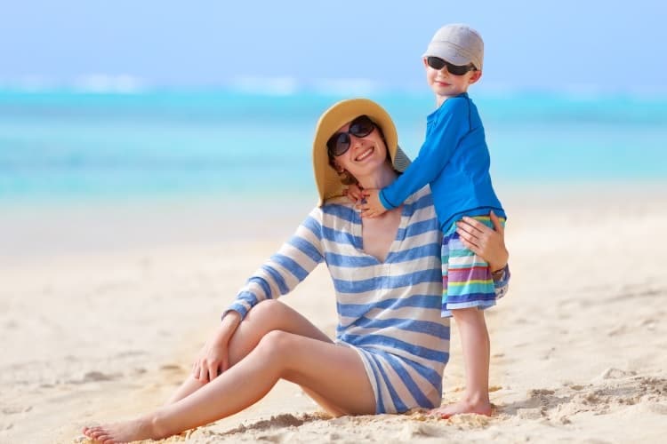 Photo of a mother and her young son wearing hats and sunglasses on the beach