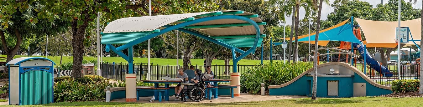 Success Stories Photo of people enjoying an outdoor picnic under a shade structure near a playground in Australia