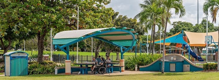 Success Stories Photo of people enjoying an outdoor picnic under a shade structure near a playground in Australia