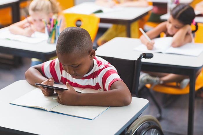 Disabled schoolboy using digital tablet School boy in a wheelchair sitting at a desk using a using digital tablet