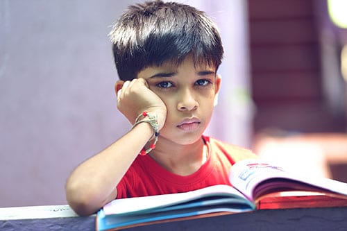 boy-posing-to-camera Young boy looking up from a book with a sad face