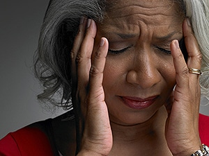 A mature woman with her head in her hands and eyes closed.