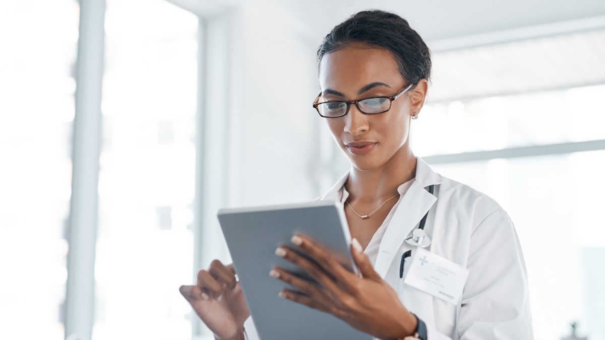 A healthcare provider wearing glasses reads a tablet in an office.