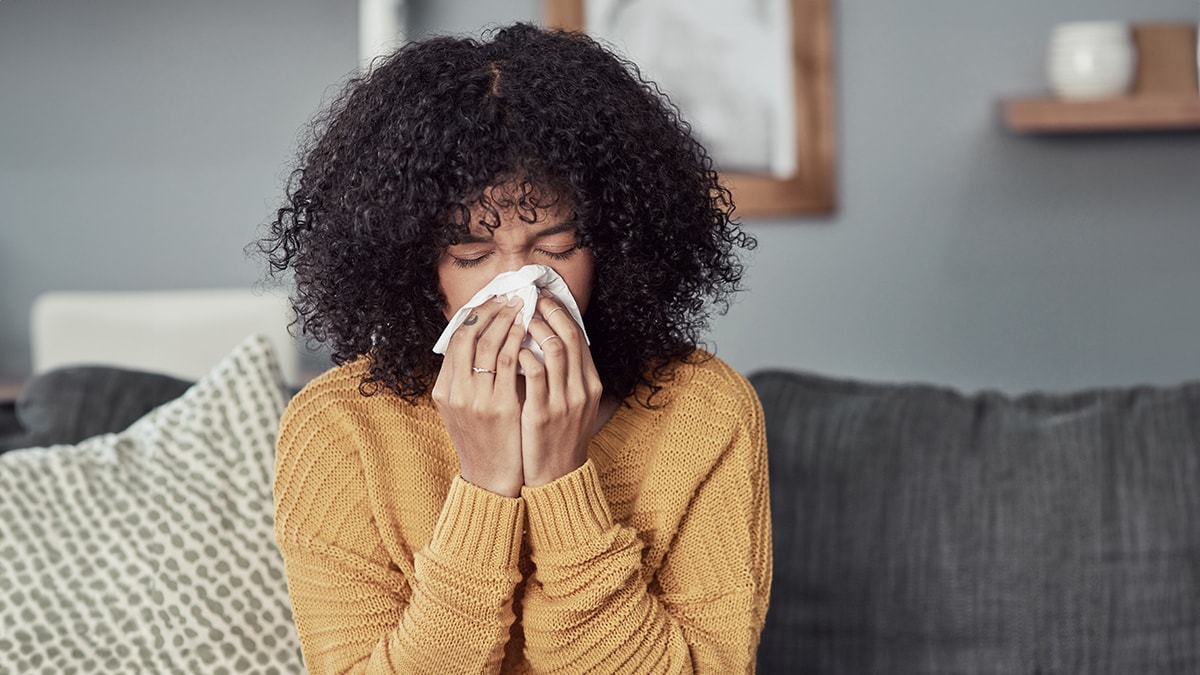 Woman blowing nose Sick woman on the couch blowing her nose.