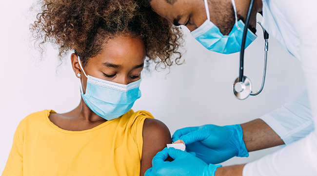 Male doctor puts a bandage on a girl’s arm after receiving immunization