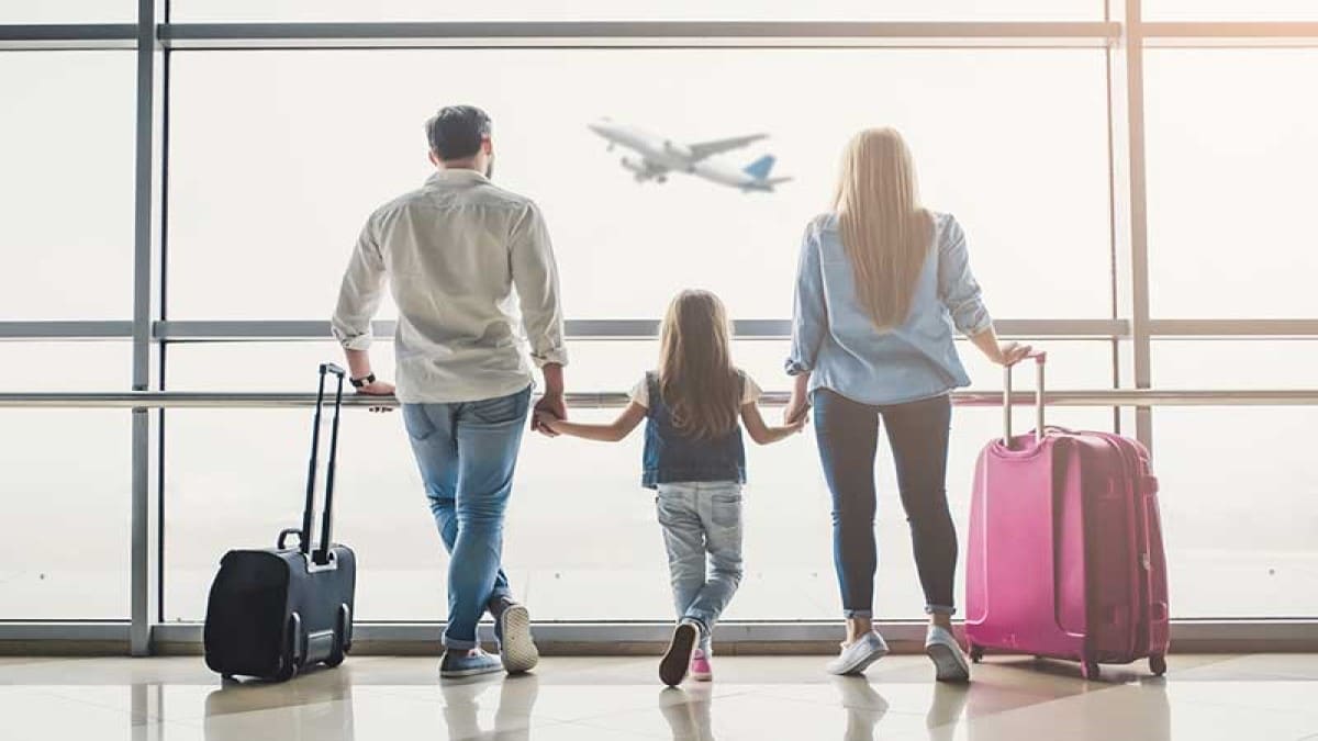 — title missing — Three people with suitcases looking at a plane in the sky.