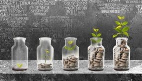 Five jars with change in each from very little money with a seedling to a full jar with a full-grown plant.