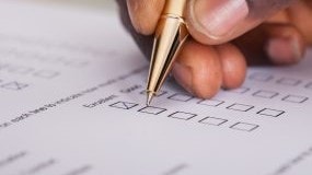 A form with blank check boxes and a hand with a pen filling in the boxes.