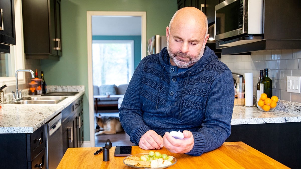 low-blood-sugar-treatment-cr Hombre comiendo un refrigerio y chequeándose el nivel de azúcar en la sangre