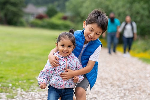 AI-family Young Native American children running on a path outdoors with their parents walking behind
