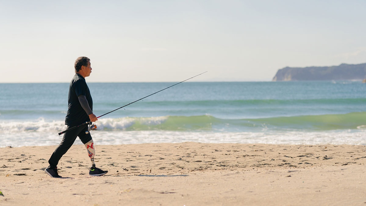 Senior man with artificial leg walking at beach with fishing rod African American woman’s feet with pink nail polish