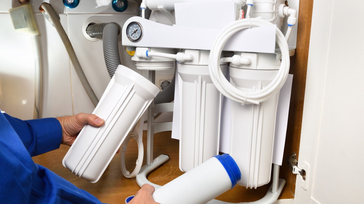 A person removes a canister from an under-sink water treatment system and prepares to put in a new filter.