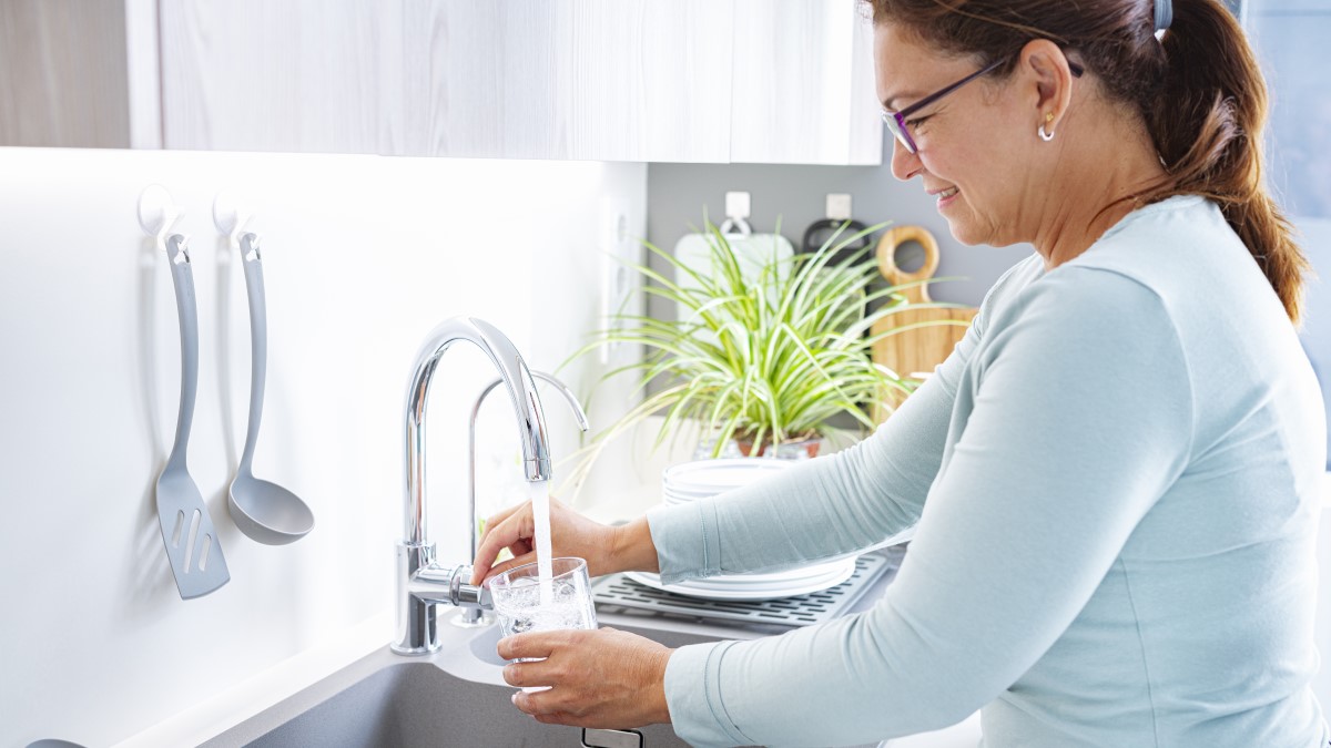 Smiling woman filling a drinking glass from the kitchen tap