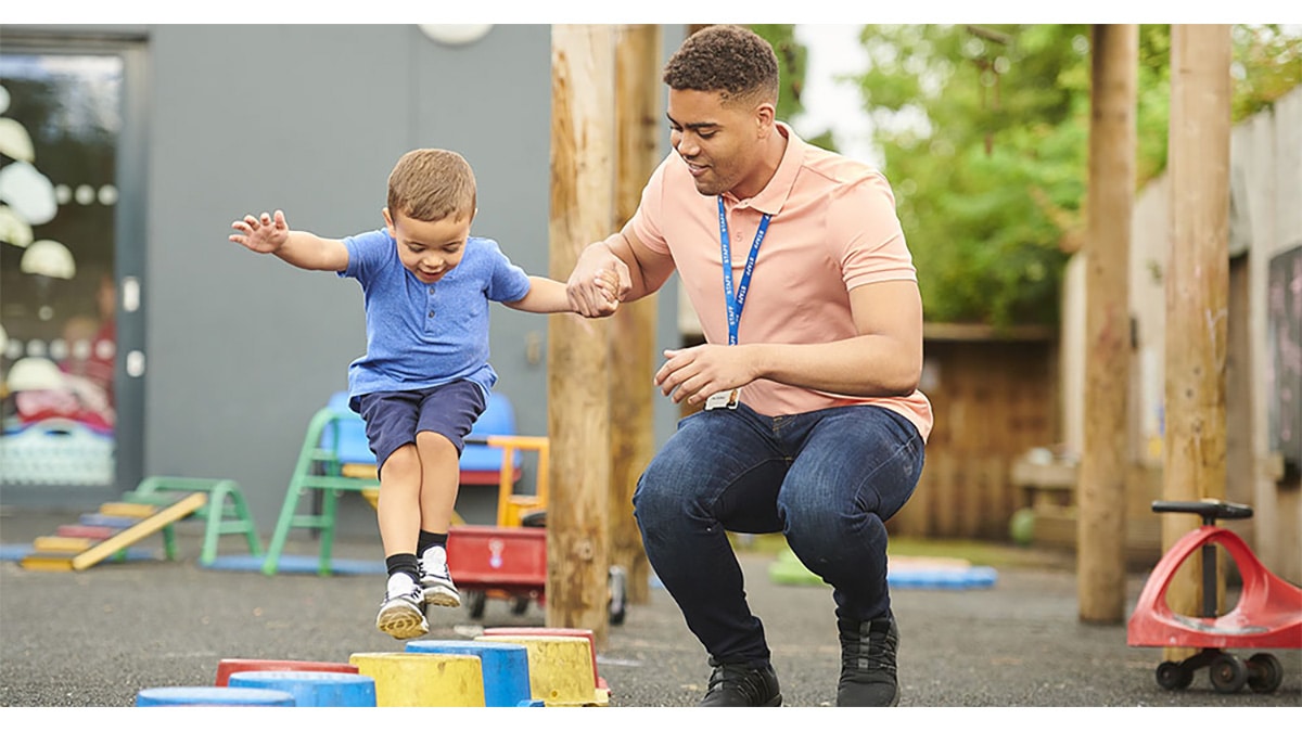 Caregiver helping boy jump An early educator helping a child jump on the playground.