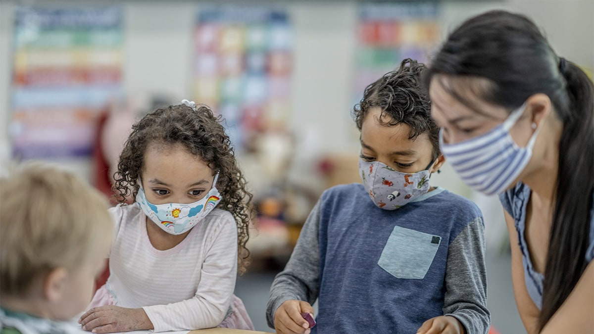 Teacher students with mask Teacher and young students wearing masks while they sit at a table together.