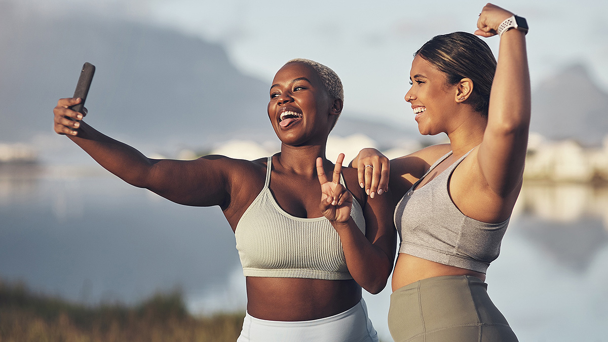 EWB Fitness Selfie An African-American and a Latina woman posing with a peace sign and flexed bicep for a happy selfie.