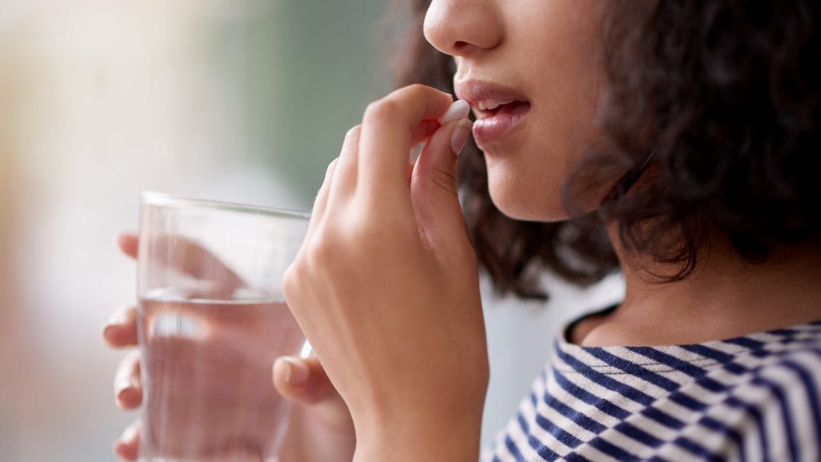 Woman taking a pill with a glass of water.