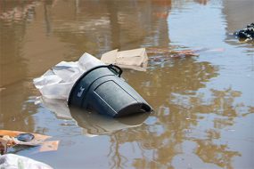  Un cubo de basura flotando en las aguas de la inundación con basura a su alrededor.