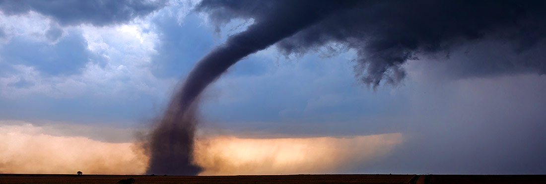 El pico de un gran tornado lanza escombros en el aire mientras cruza un campo abierto The spout of a large tornado throws debris in the air as it crosses an open field