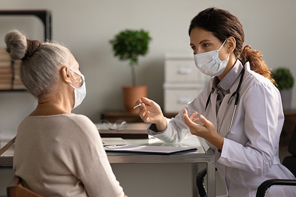 Close up serious doctor wearing mask consulting mature woman patient A female doctor talking with elder patient and both wearing masks.