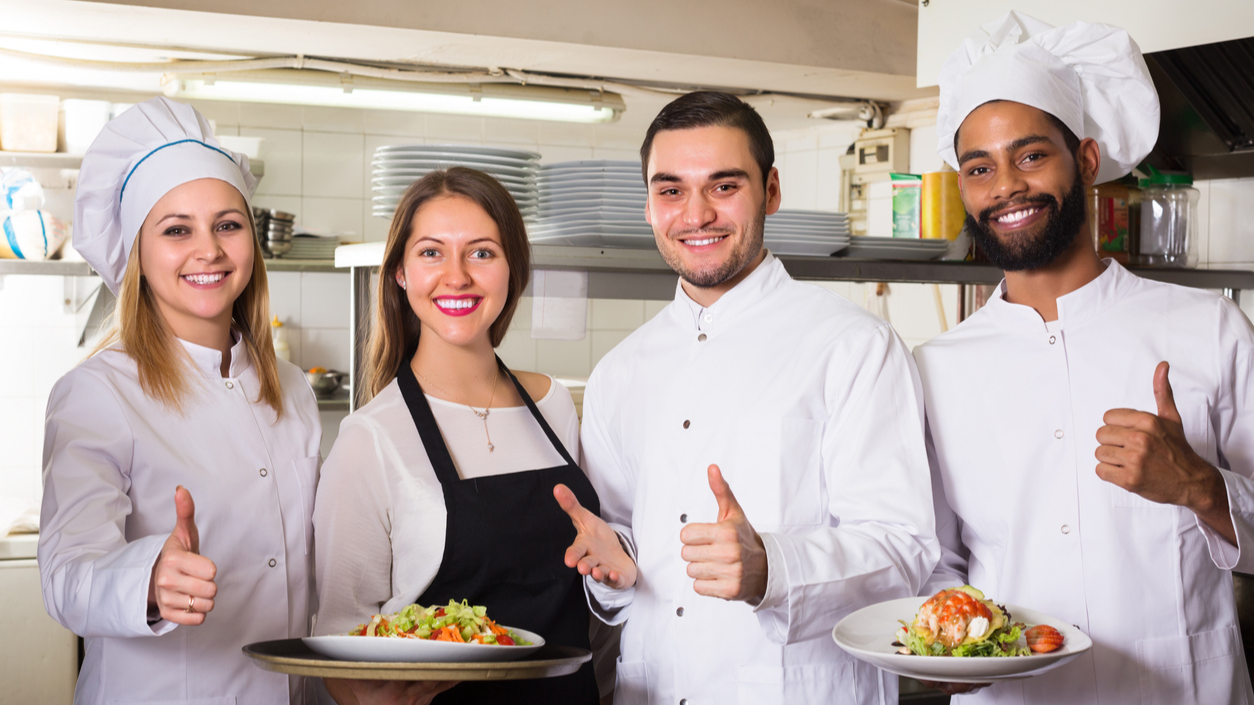Four chefs or kitchen staff with healthy food giving a "thumbs up" sign.