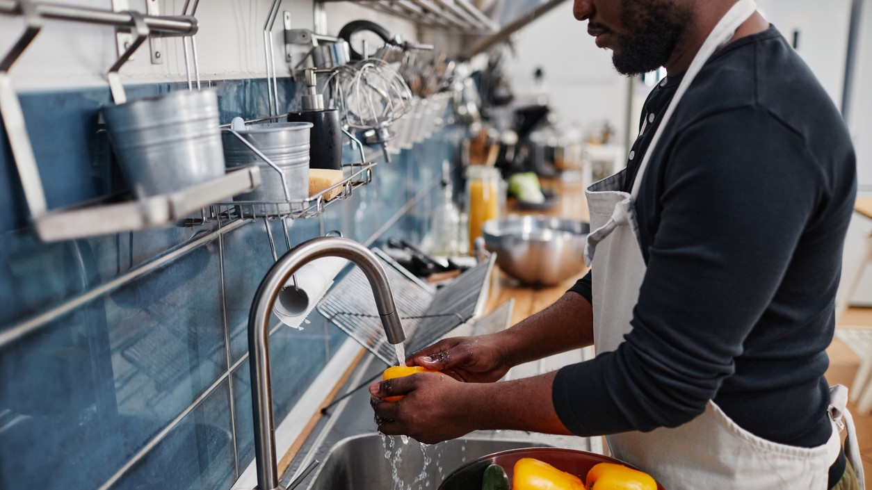 Man in commercial kitchen washing vegetables.