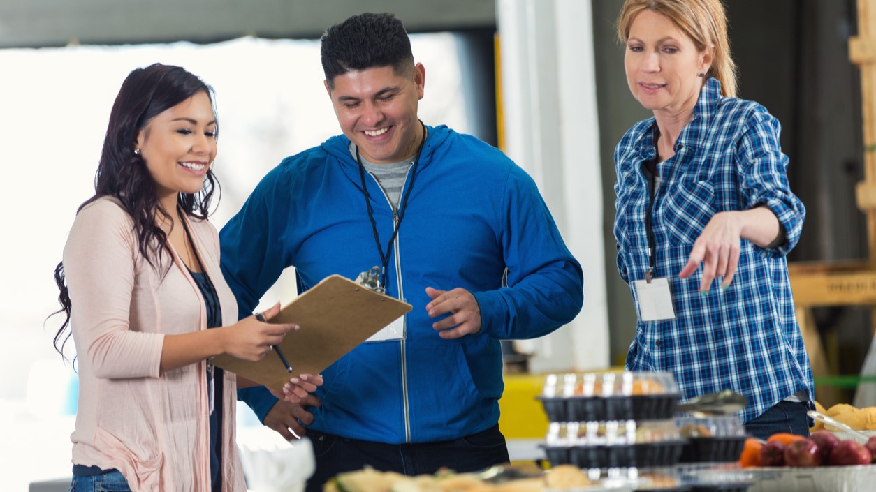 Three people checking foods served in a cafeteria.