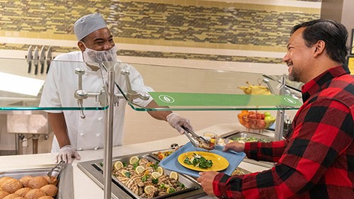 Food service worker serving man in cafeteria line.