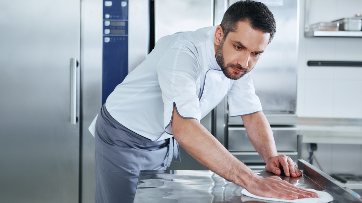 Man cleaning worktable in commercial kitchen.