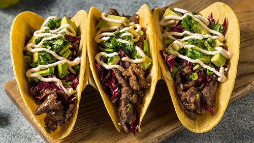 Three tacos with steak, cabbage, avocado, and more.