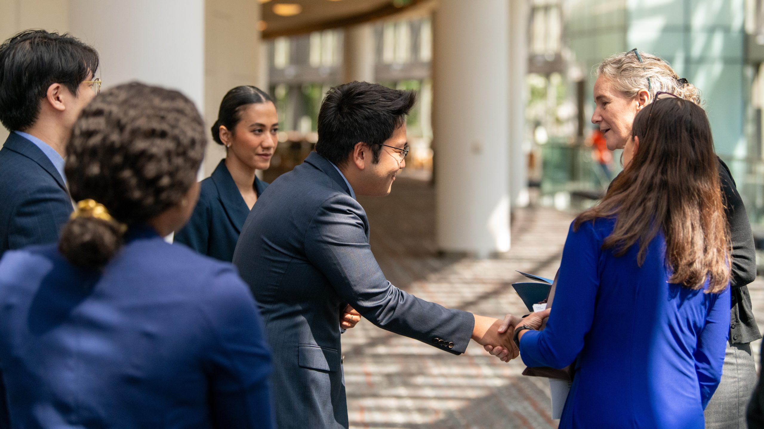 Partners-1 A group of men and women of all ethnicities standing in a group while two members shake hands