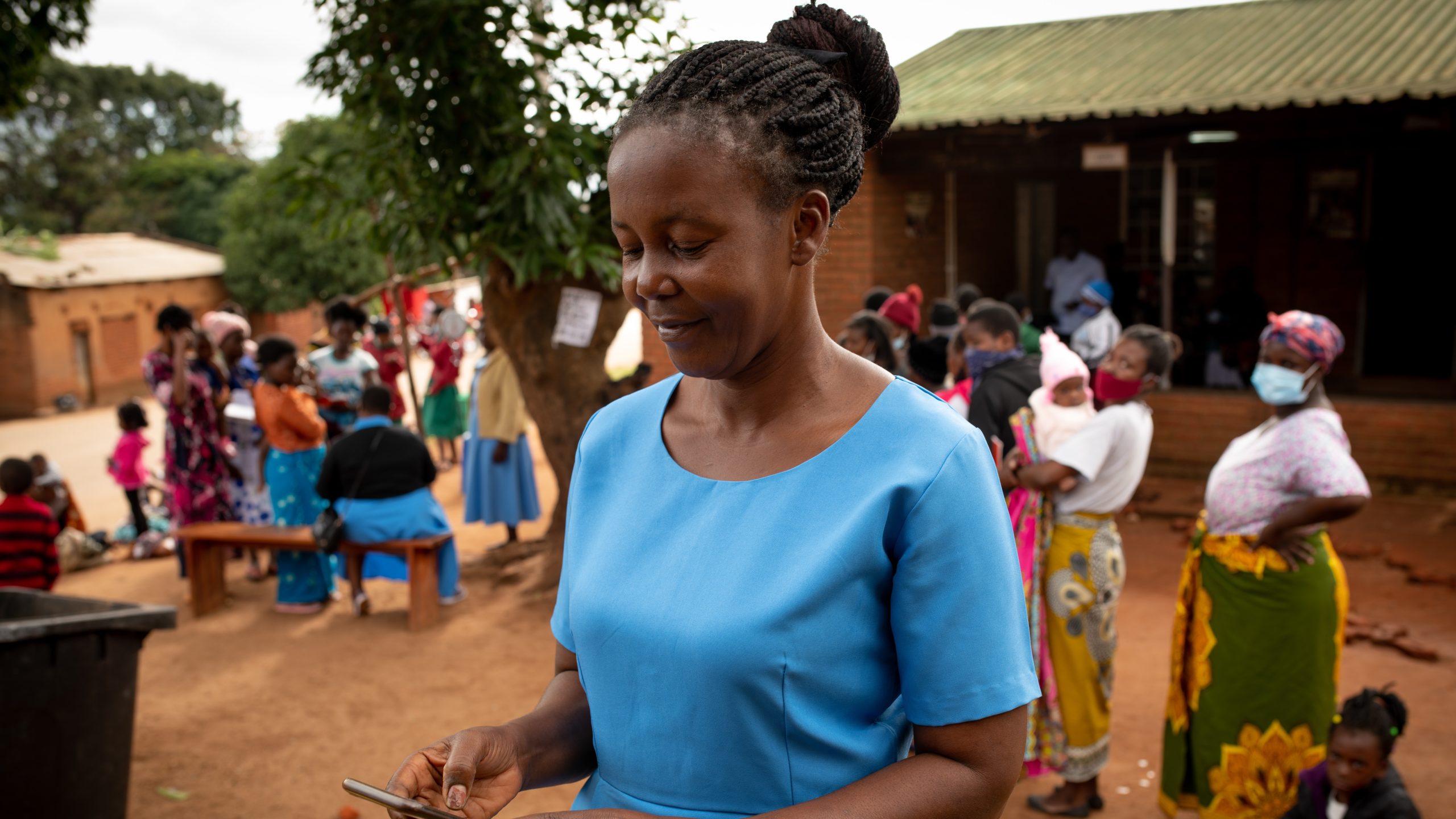Programs-Survelliance A woman in an African village smiling looking down at a phone.