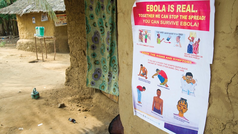 Liberia Poster An Ebola awareness poster on a mud wall in a rural setting, detailing symptoms and prevention.