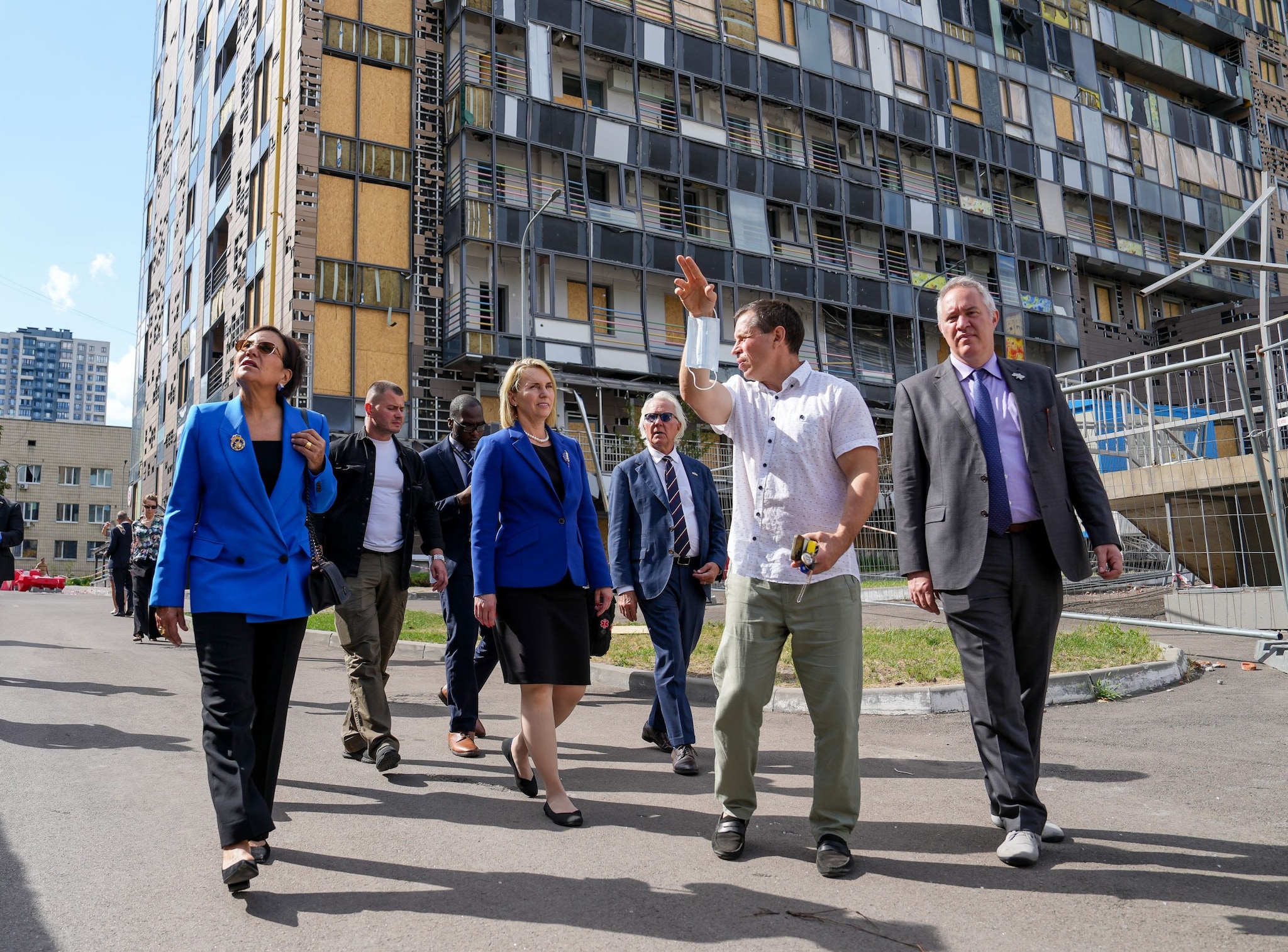 Ukraine Hospital A group of officials walking outdoors near a damaged building.