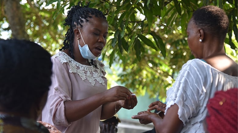 DRC_COVID-19_FieldPhoto_2022 A person hands something to another person during an outdoor village assembly in DRC